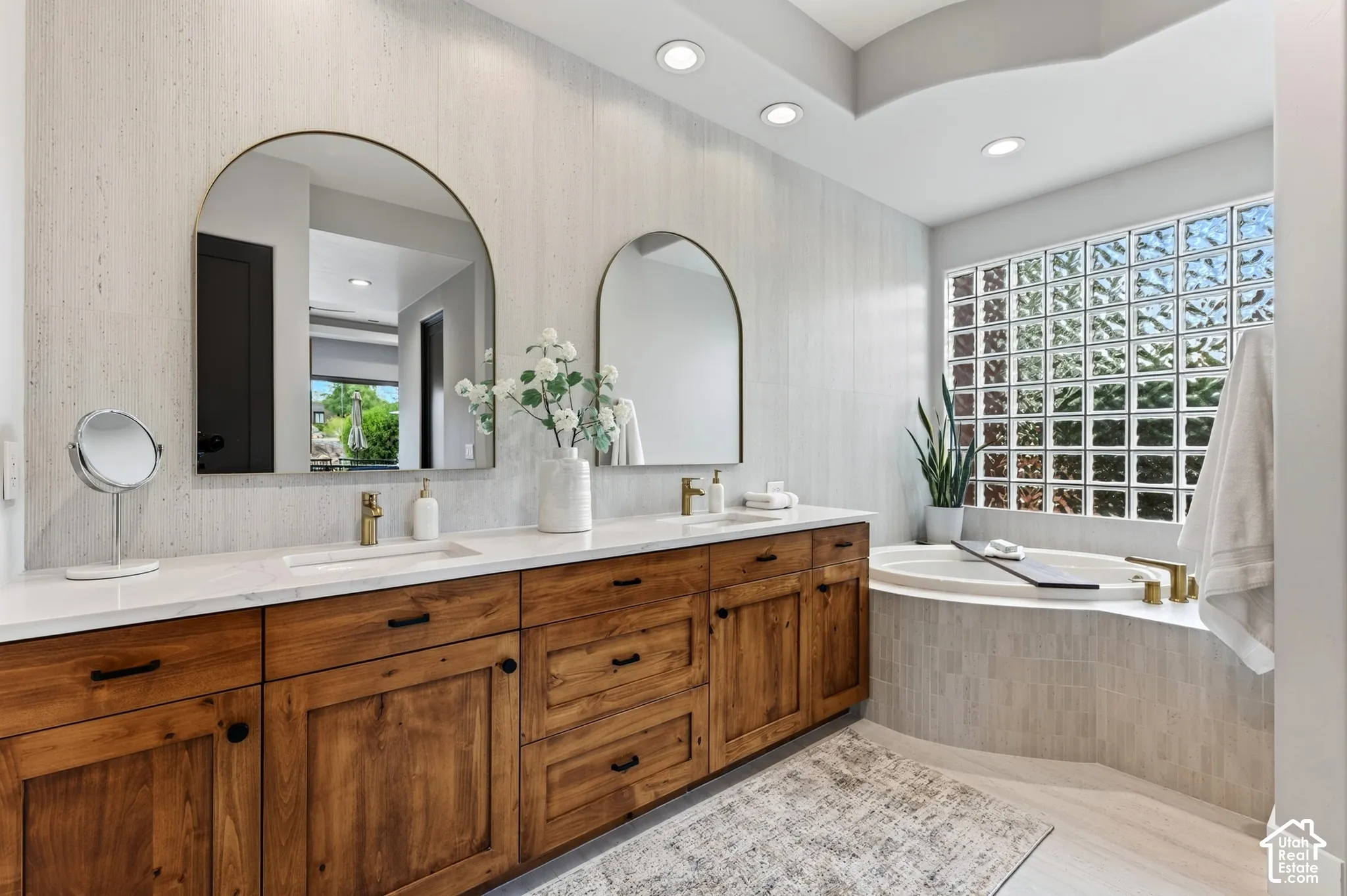 Primary Bathroom:  Dual arched mirrors, expansive double vanity with wood-finish cabinetry, built-in soaking tub, glass block privacy window, and recessed lighting