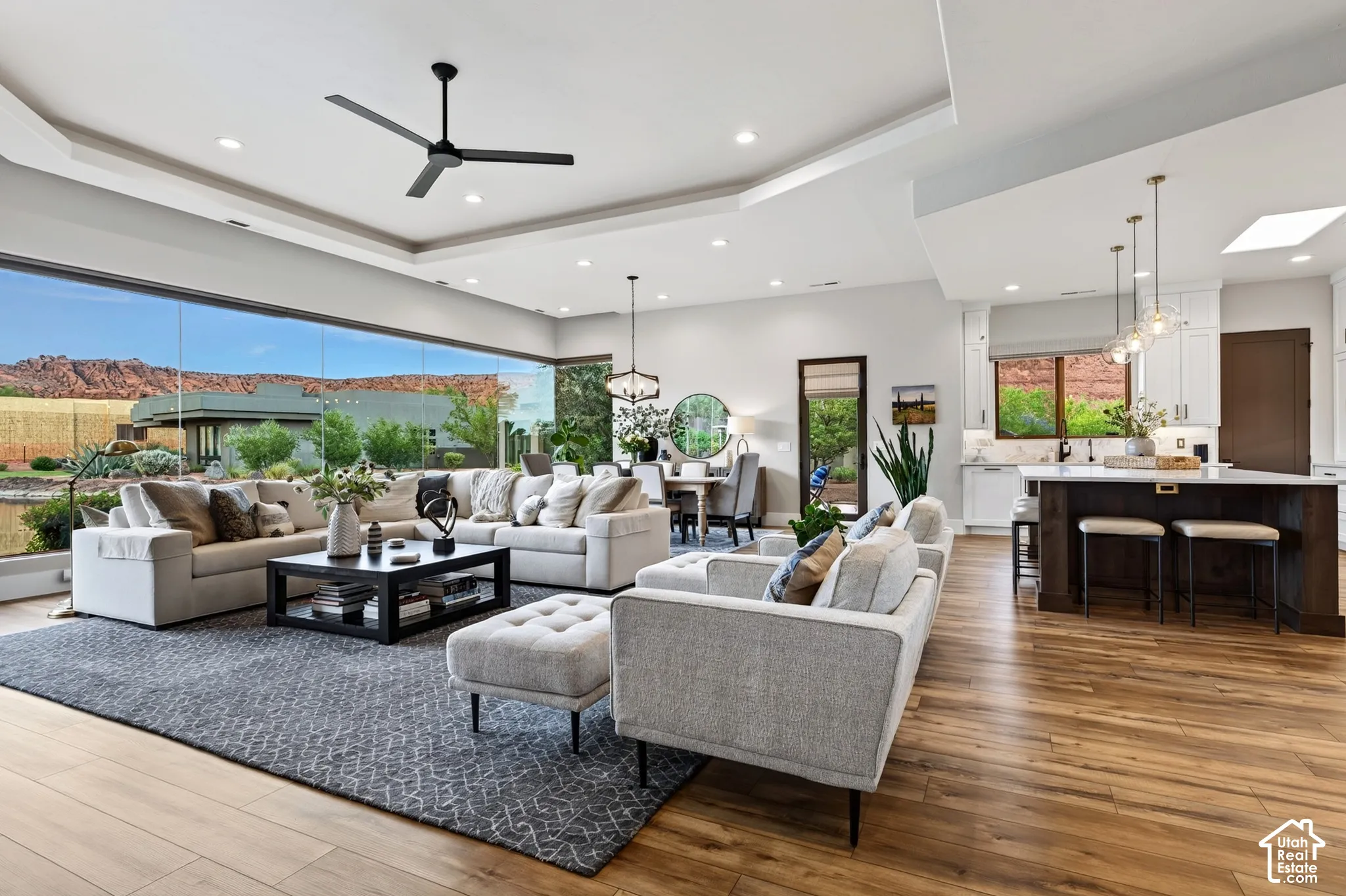 Expansive living area featuring wood-finish flooring, a tray ceiling, and a contemporary ceiling fan