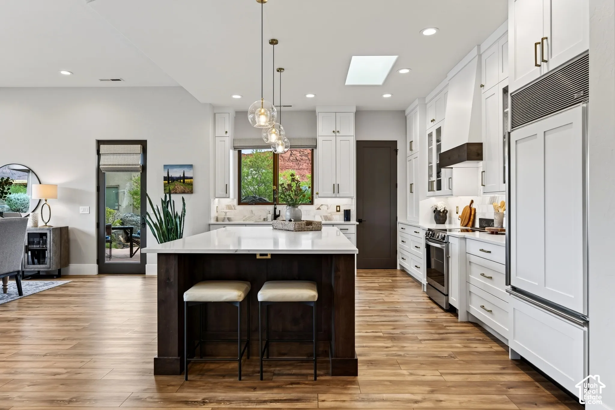 Gourmet kitchen featuring white cabinetry, professional-grade appliances, a large center island with seating, a skylight, and wood-finish flooring