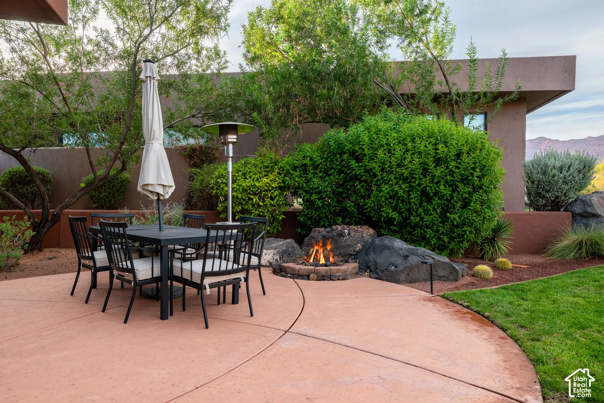 Expansive patio area with concrete surfacing, a built-in fire pit, and mature landscaping