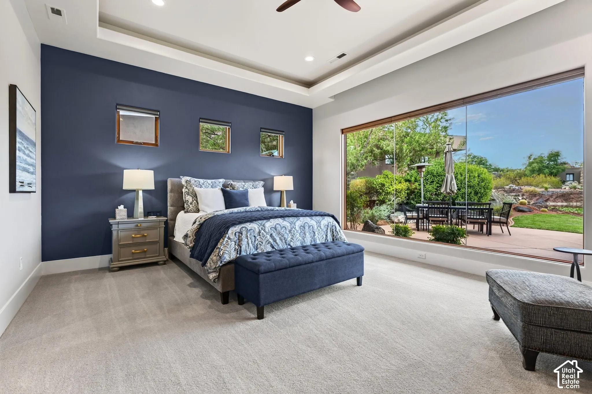Primary Bedroom:  Expansive full-height glass paneling, tray ceiling with recessed lighting, plush carpeting, and a private outdoor patio with hardscaping