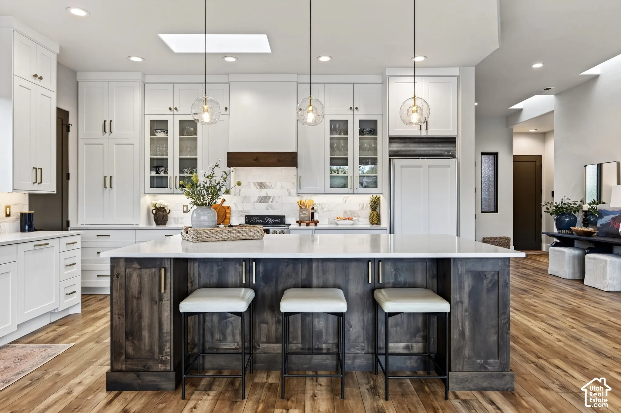 Spacious kitchen featuring white cabinetry, a large wood-finish island with seating, a white countertop, and wood-finish flooring