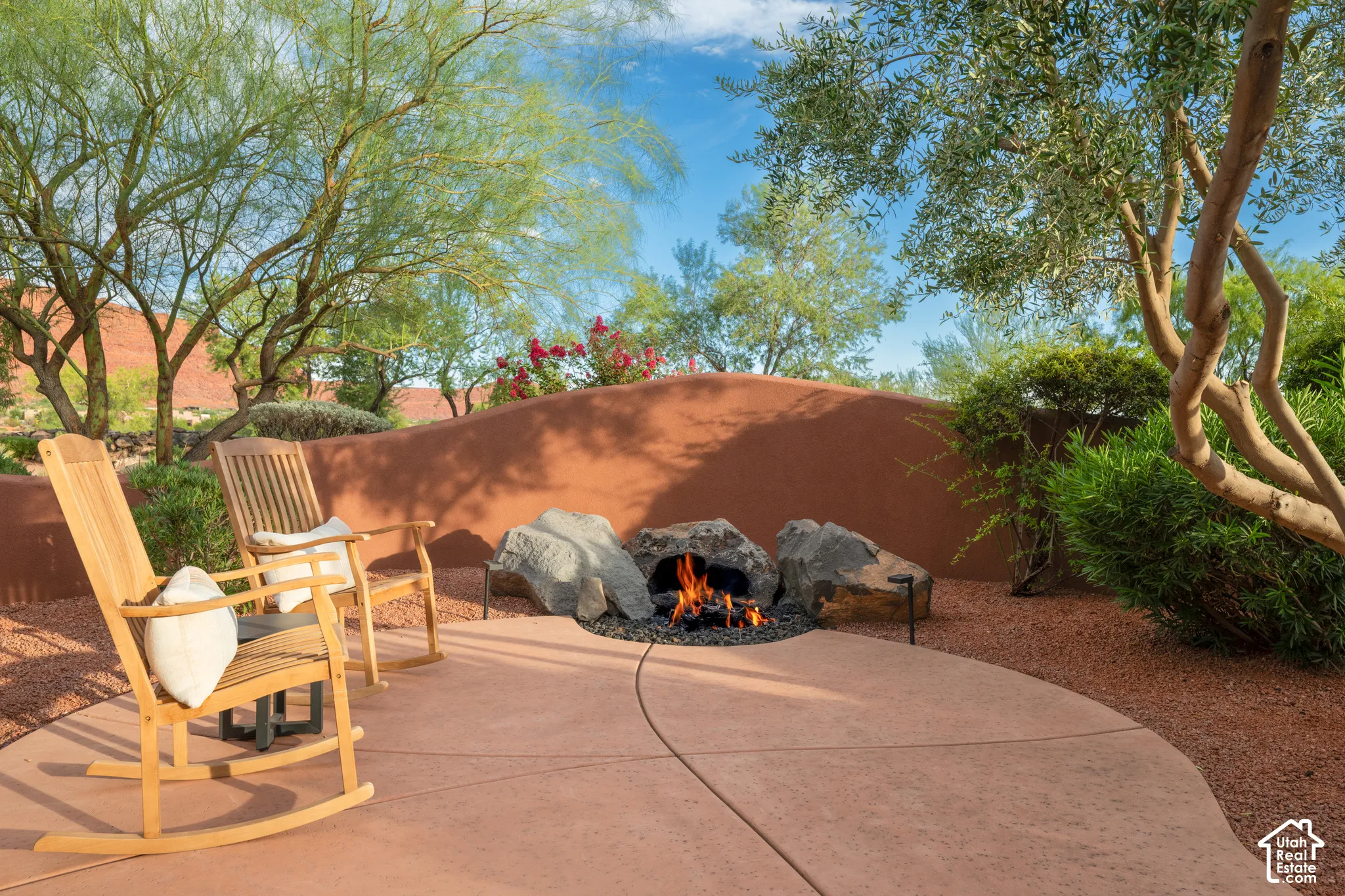 Casita / Entry Patio: Curved concrete patio with a built-in fire pit surrounded by large stones, complemented by desert landscaping and mature trees