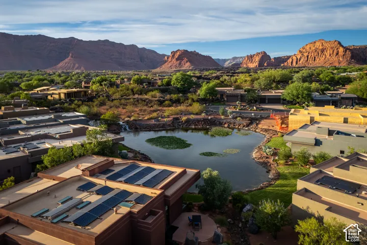 Rooftop solar panels, surrounding natural rock formations, natural water feature, verdant landscaping, and a patio area