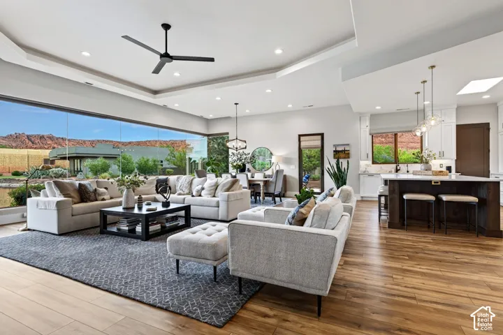 Expansive living area featuring wood-finish flooring, a tray ceiling, and a contemporary ceiling fan