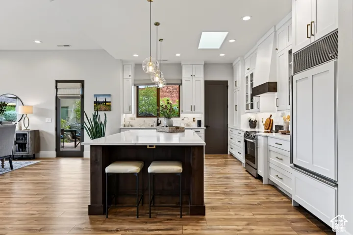 Gourmet kitchen featuring white cabinetry, professional-grade appliances, a large center island with seating, a skylight, and wood-finish flooring