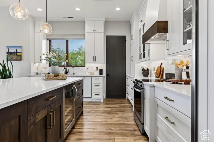 Kitchen featuring white cabinetry with dark hardware, a center island with a built-in beverage cooler, wood-finish flooring, and a window above the sink