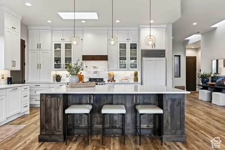 Spacious kitchen featuring white cabinetry, a large wood-finish island with seating, a white countertop, and wood-finish flooring
