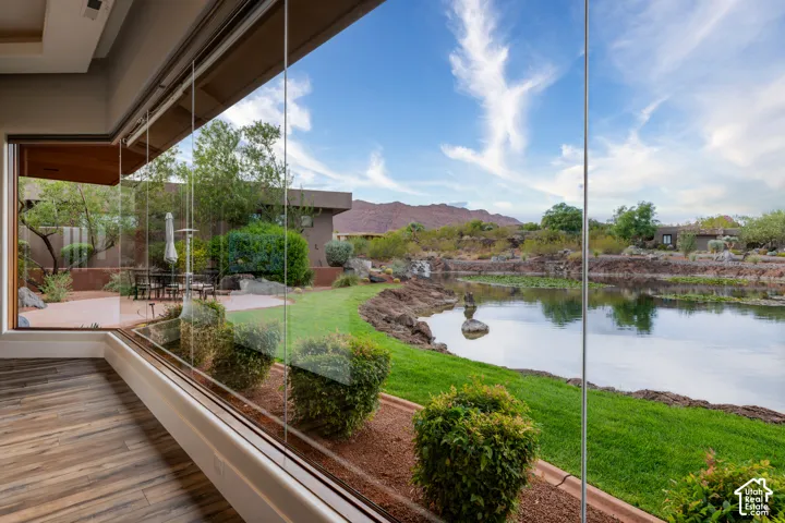 Expansive glass wall system, wood-finish flooring, private patio, manicured lawn, and natural water feature
