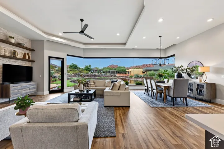 Expansive window wall, wood-finish flooring, tray ceiling with recessed lighting, built-in shelving, and a modern ceiling fan