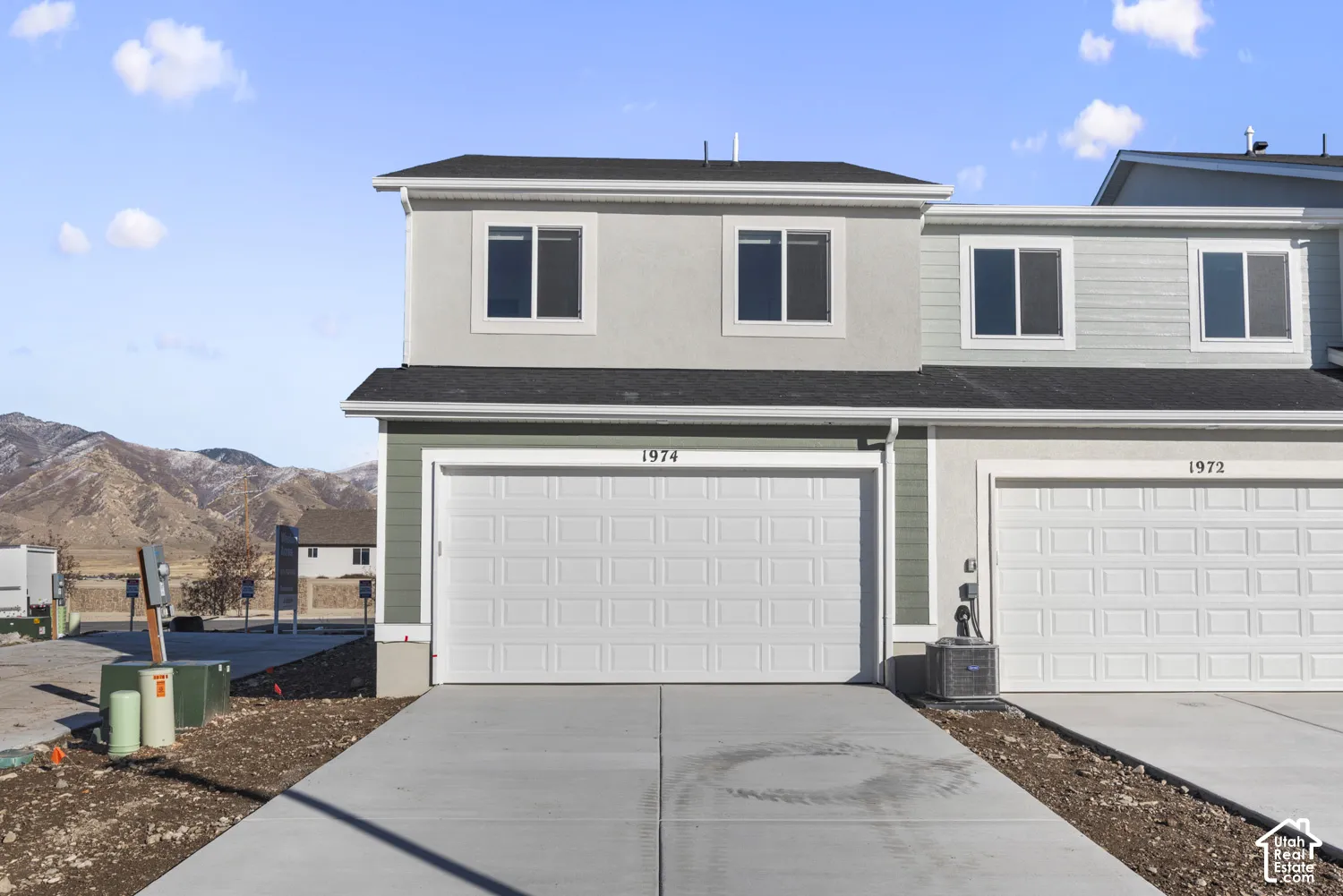 Two-story exterior with light gray stucco and green siding accents, two attached garages with white panel doors, and a concrete driveway