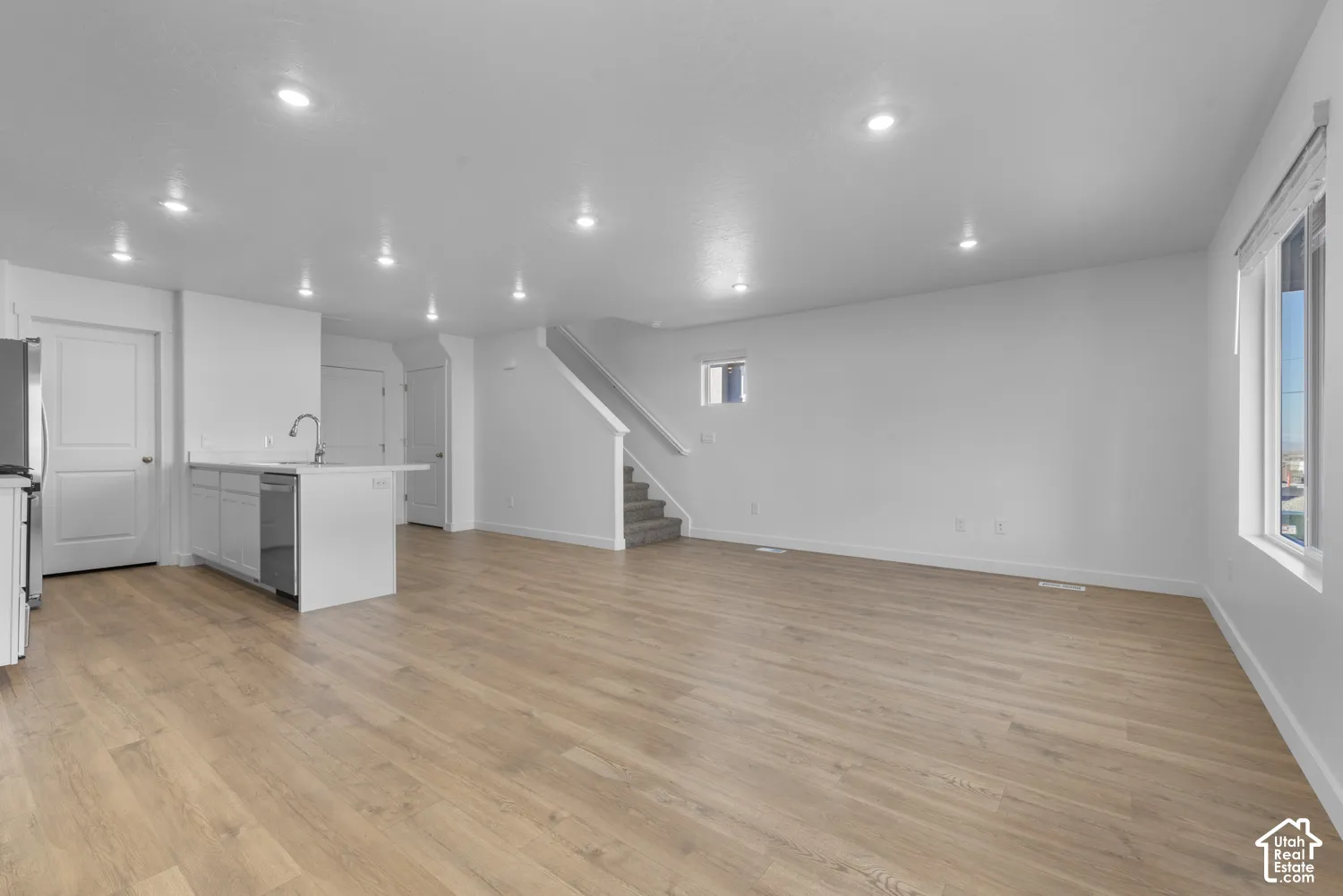 Open-concept living area with wood-finish flooring, white walls, recessed lighting, and a kitchen island with an undermount sink
