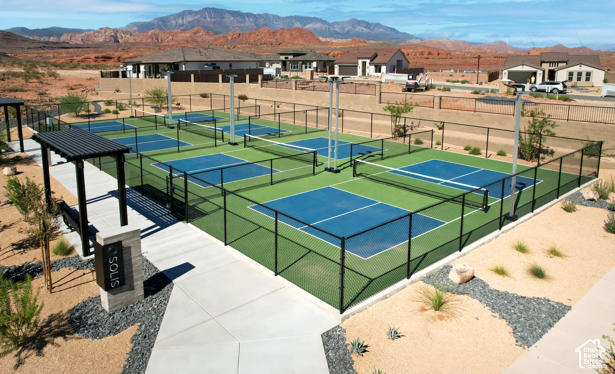 Multiple fenced pickleball courts, covered seating structure, and hardscaping with drought-tolerant plantings