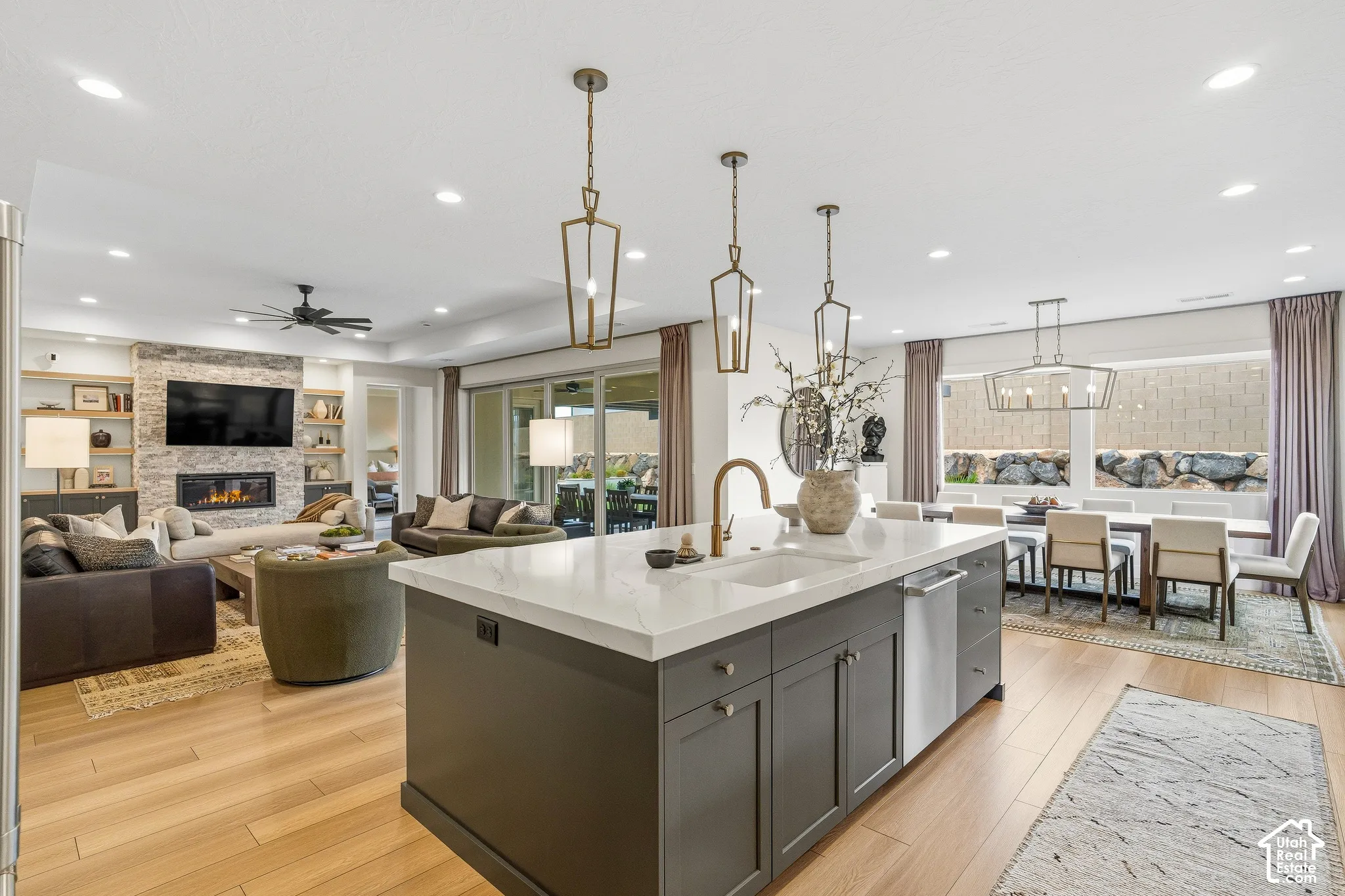 Kitchen island with white countertop and integrated sink, recessed lighting, wood-finish flooring, stone-clad fireplace with built-in shelving, and large sliding glass doors