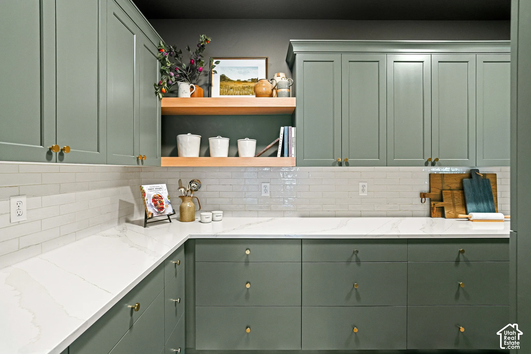 White subway tile backsplash, custom cabinetry with gold-tone hardware, polished countertops, and integrated floating shelves