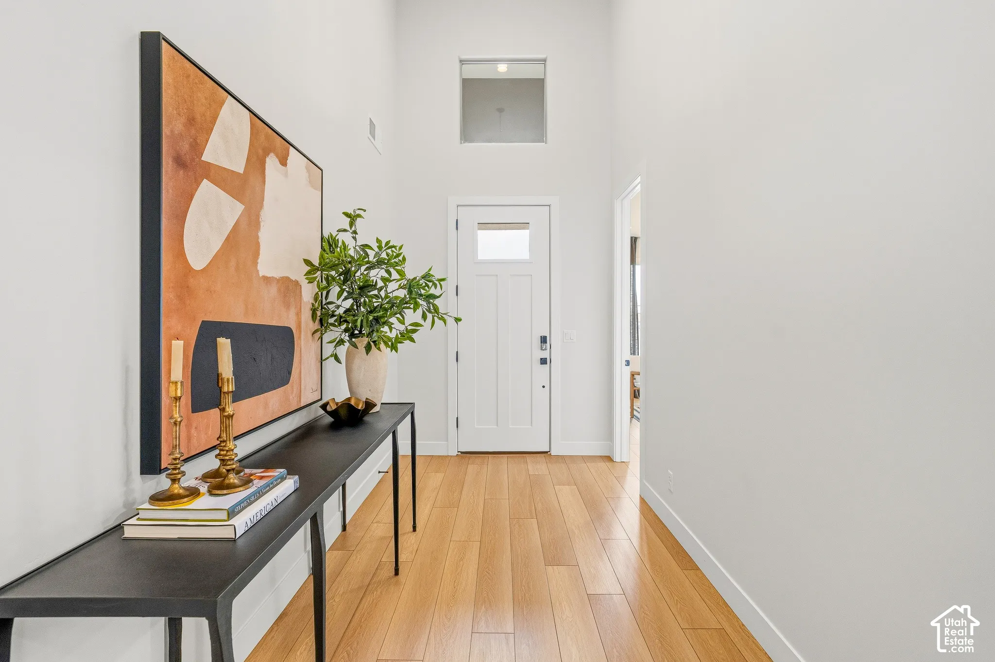 High ceilings, light wood-finish flooring, white walls, transom window, and a white paneled door