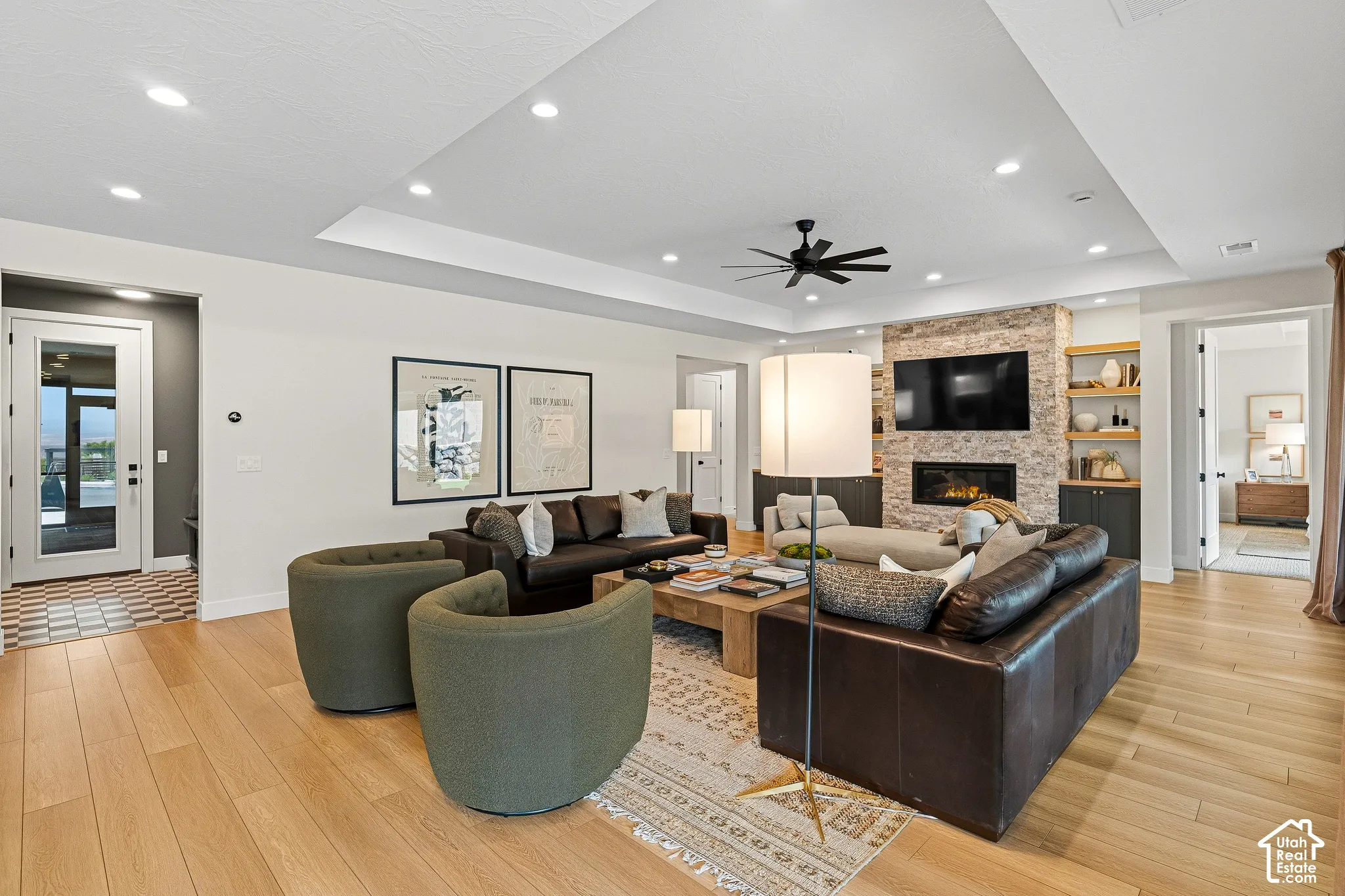 Spacious living area featuring wood-finish flooring, a stone-clad fireplace, integrated shelving, and a tray ceiling with recessed lighting