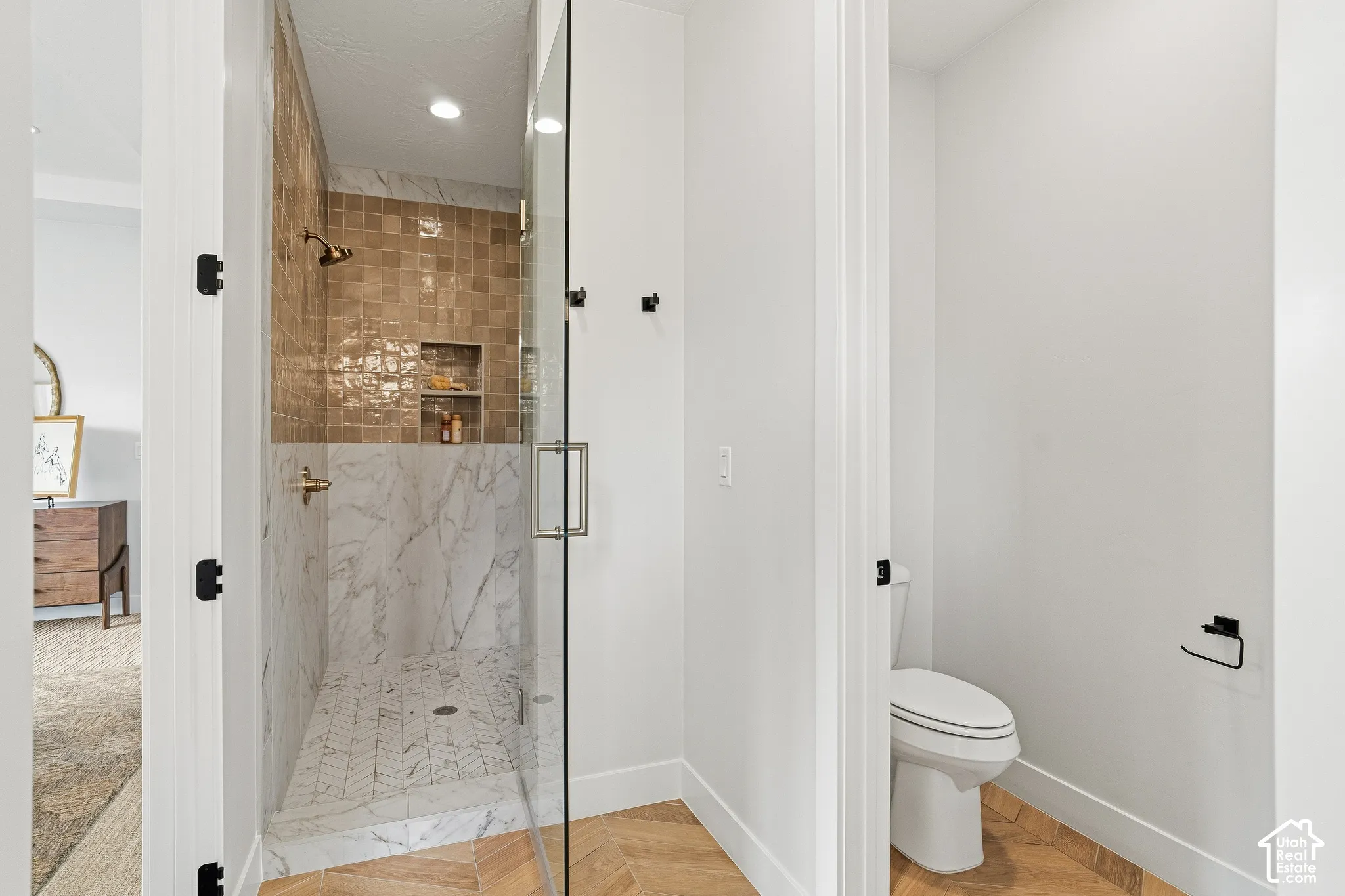 Glass-enclosed shower with a marble-patterned tile surround, recessed niche, and gold-toned fixtures