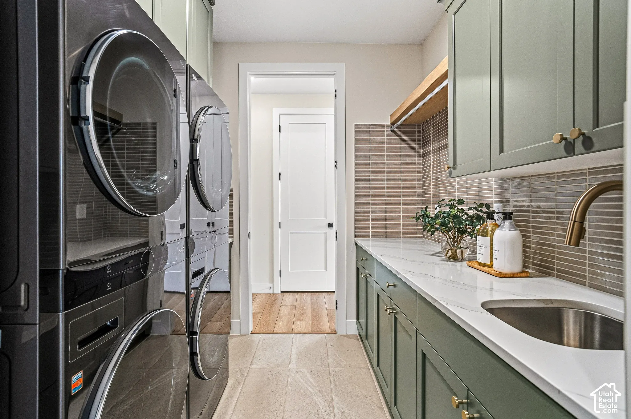 Laundry space featuring a stackable washer and dryer, an undermount sink, green shaker-style cabinetry, and a tile backsplash