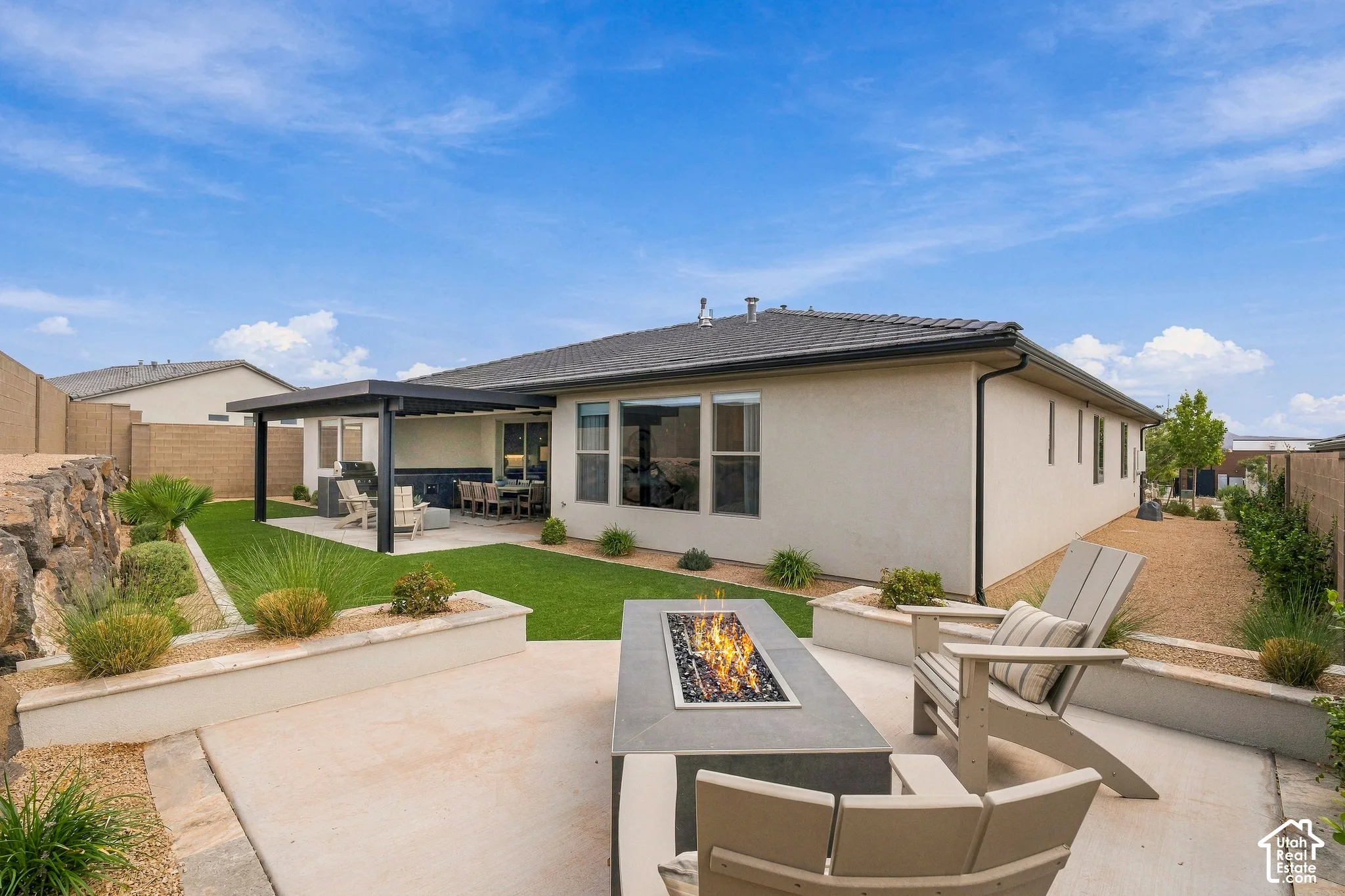 Expansive concrete patio featuring a built-in fire pit, covered outdoor living area, and a low-maintenance artificial turf lawn