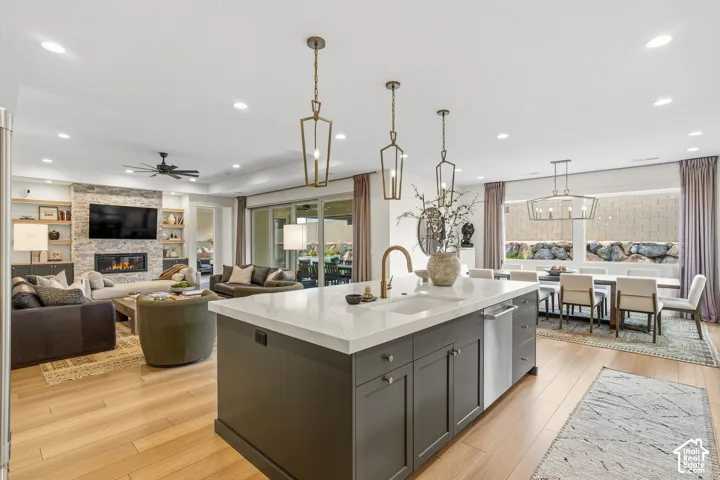Kitchen island with white countertop and integrated sink, recessed lighting, wood-finish flooring, stone-clad fireplace with built-in shelving, and large sliding glass doors