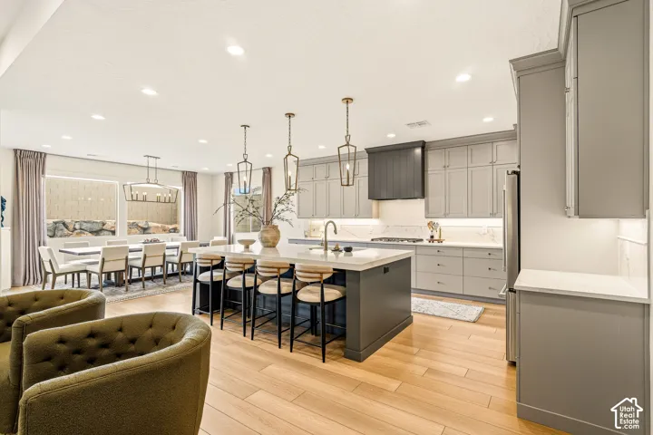 Open concept kitchen with a central island, light wood-finish flooring, recessed lighting, gray cabinetry, and a built-in stainless steel refrigerator