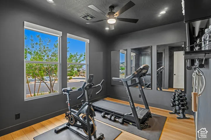Room featuring two windows with roller shades, wood-finish flooring, a ceiling fan with integrated lighting, and recessed lighting