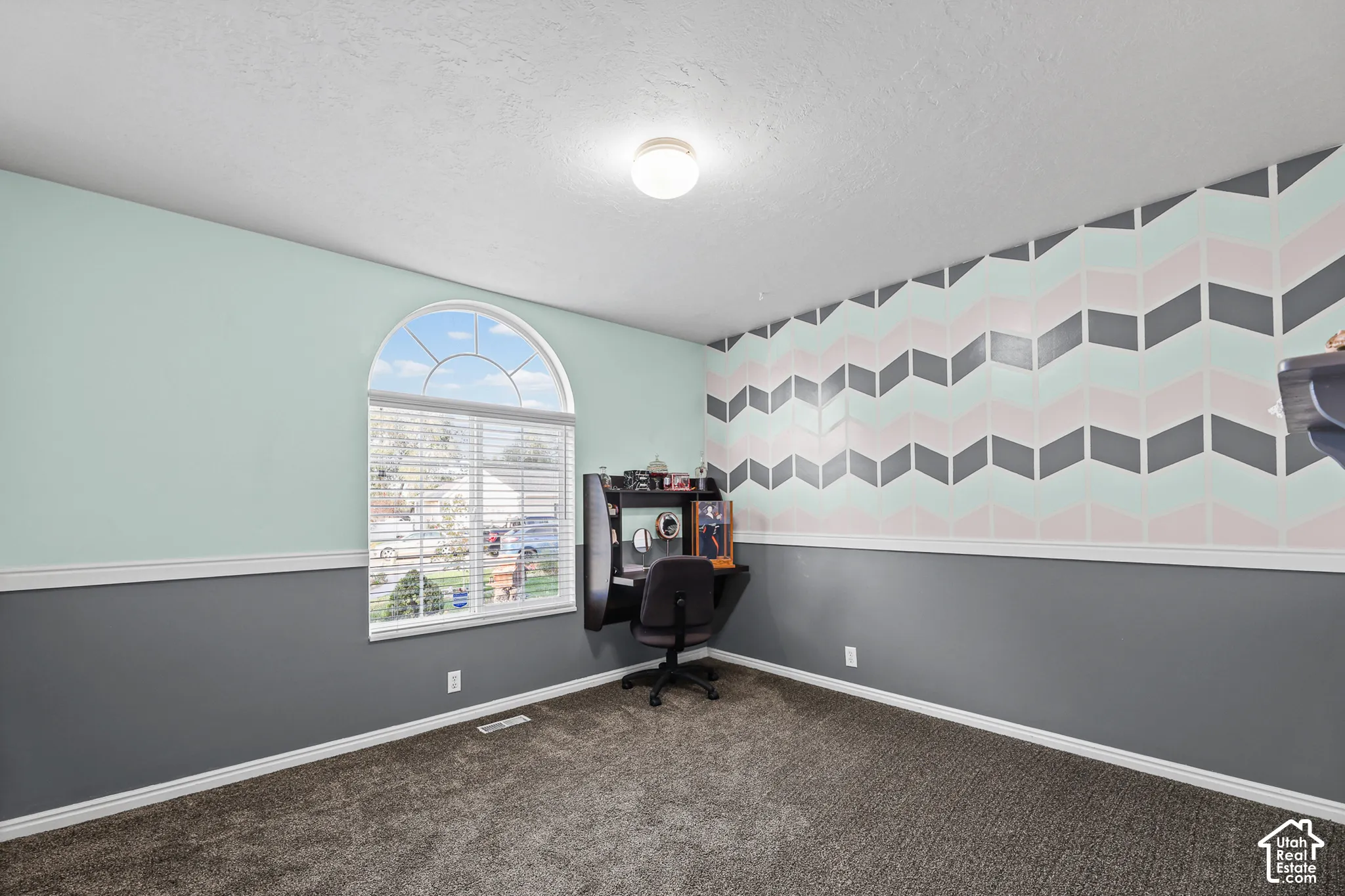Arched window with blinds, patterned accent wall, plush carpeting, and overhead flush-mount lighting