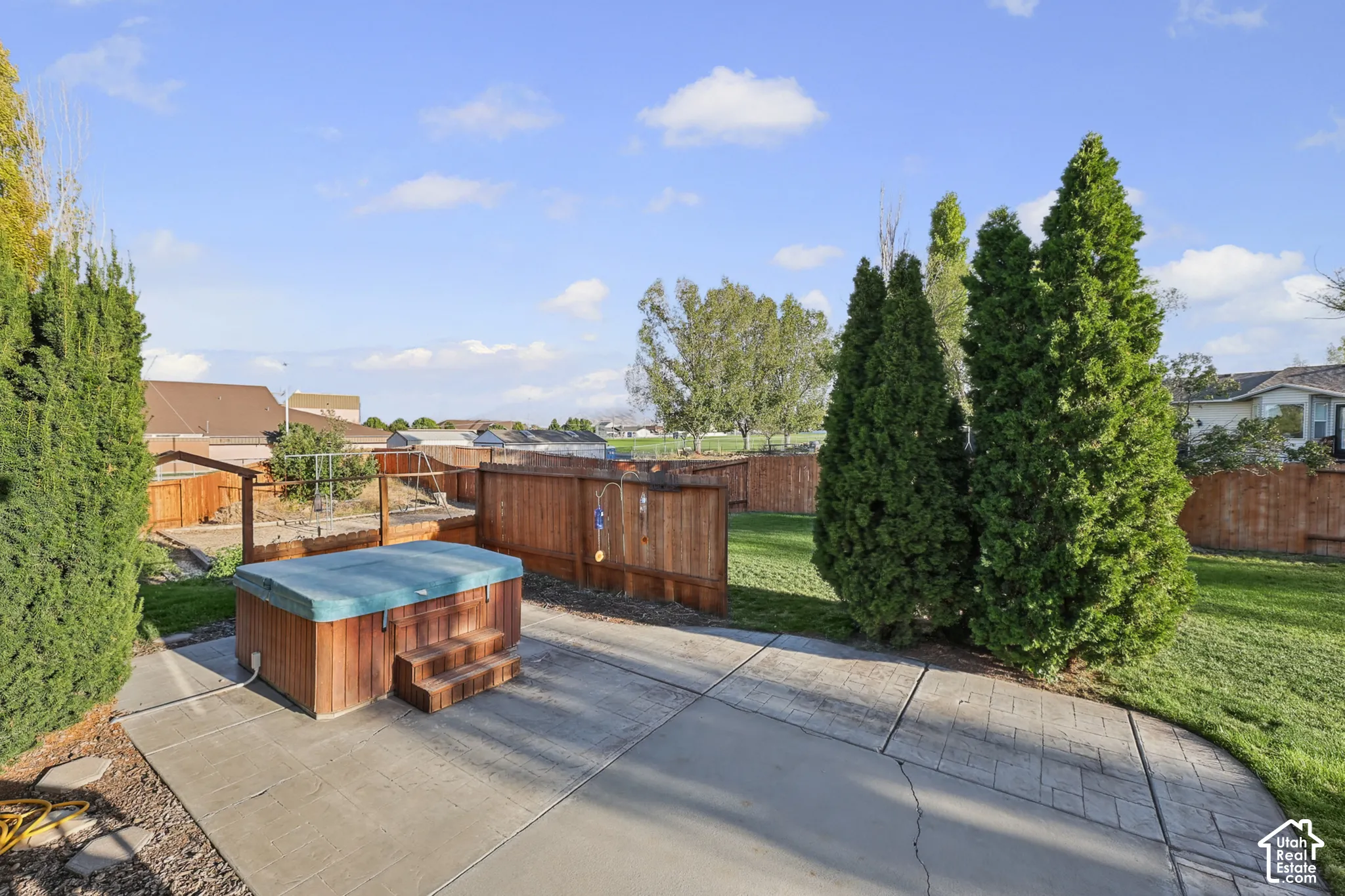 Backyard featuring a hot tub with wood surround, concrete patio, expansive lawn area, mature privacy trees, and wood fencing