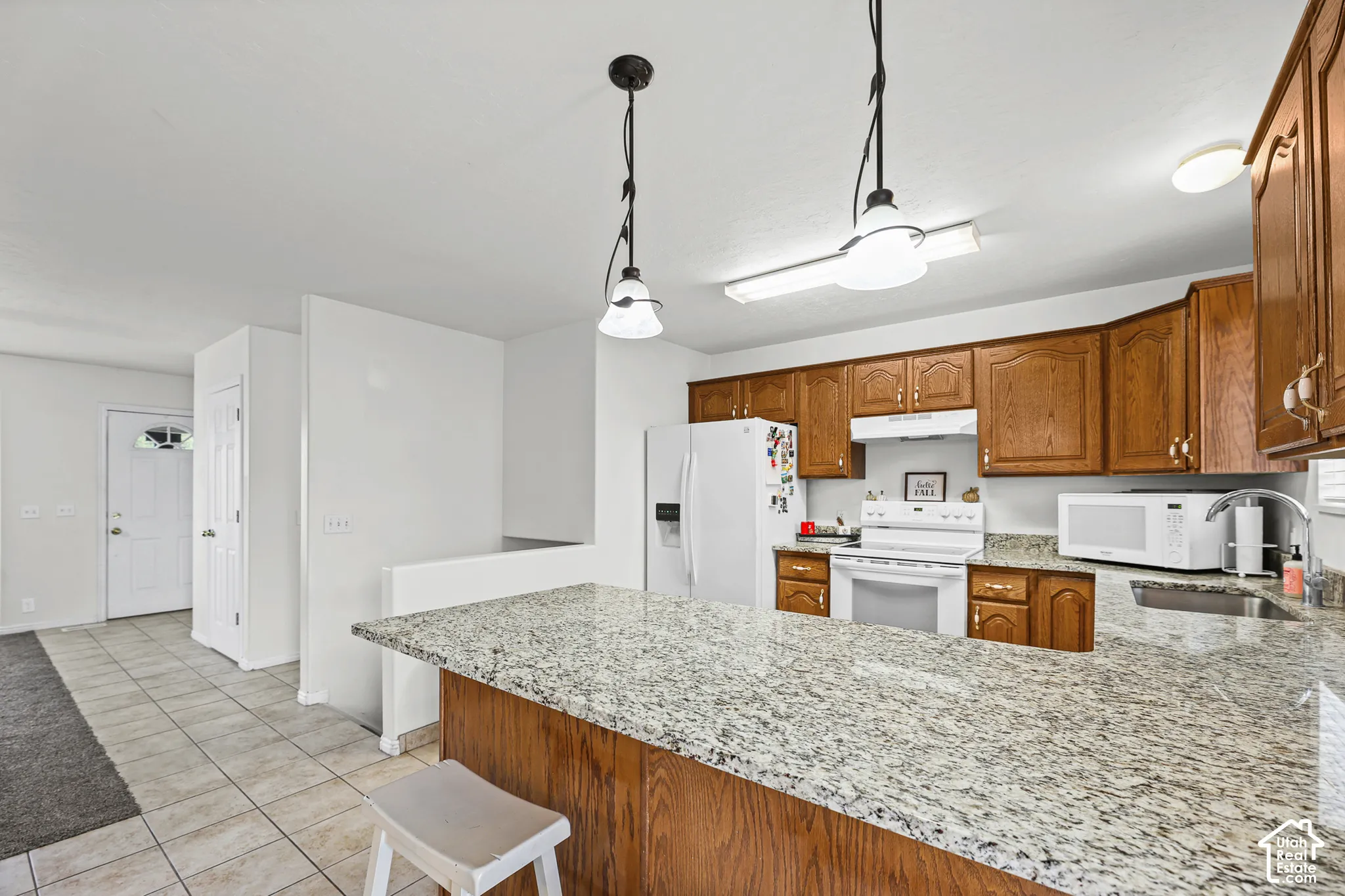 Kitchen featuring wood cabinetry, light-toned granite-style countertops, tile flooring, and white appliances