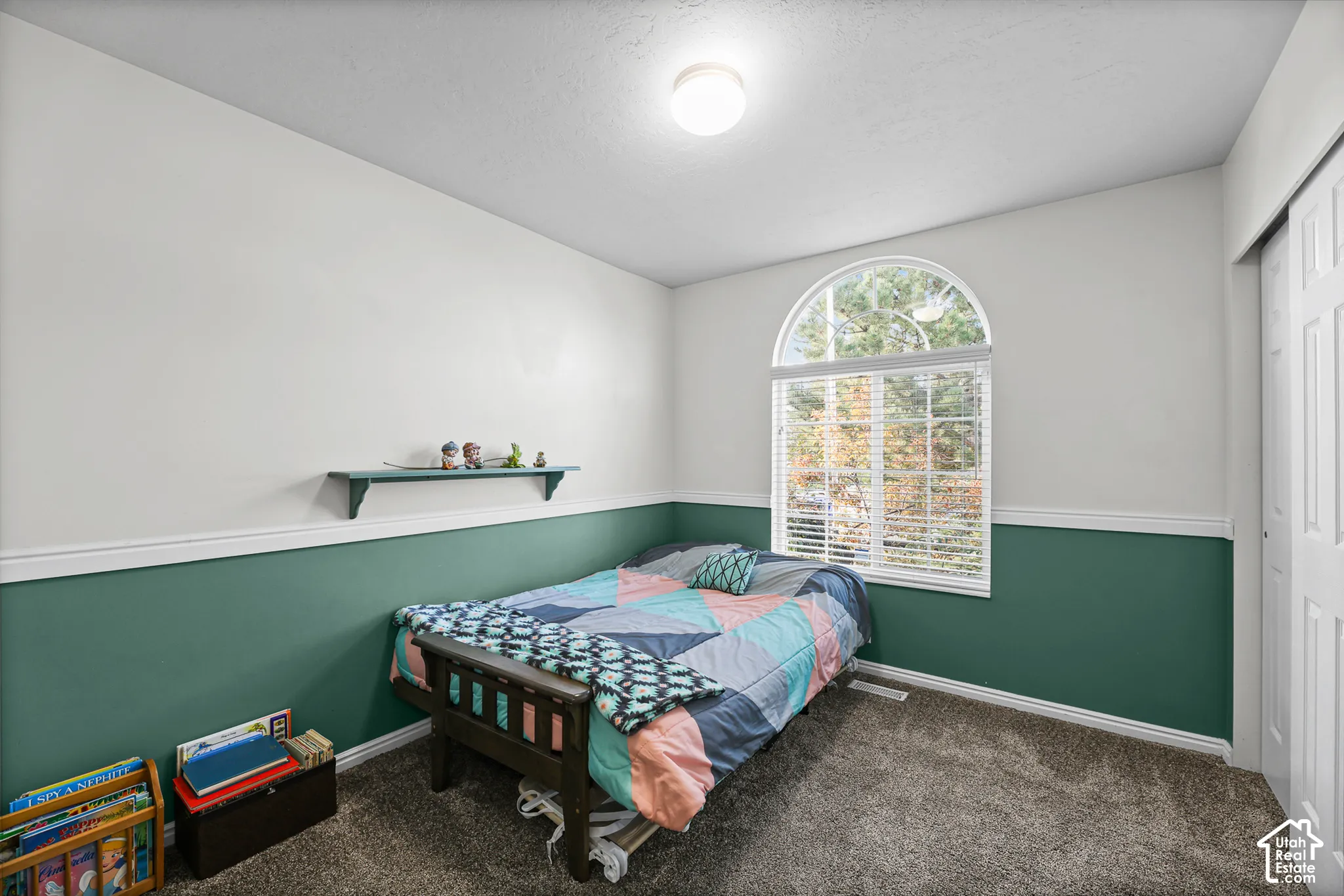 Arched window with blinds, two-tone painted walls, wall molding, built-in wall shelf, and textured carpet flooring