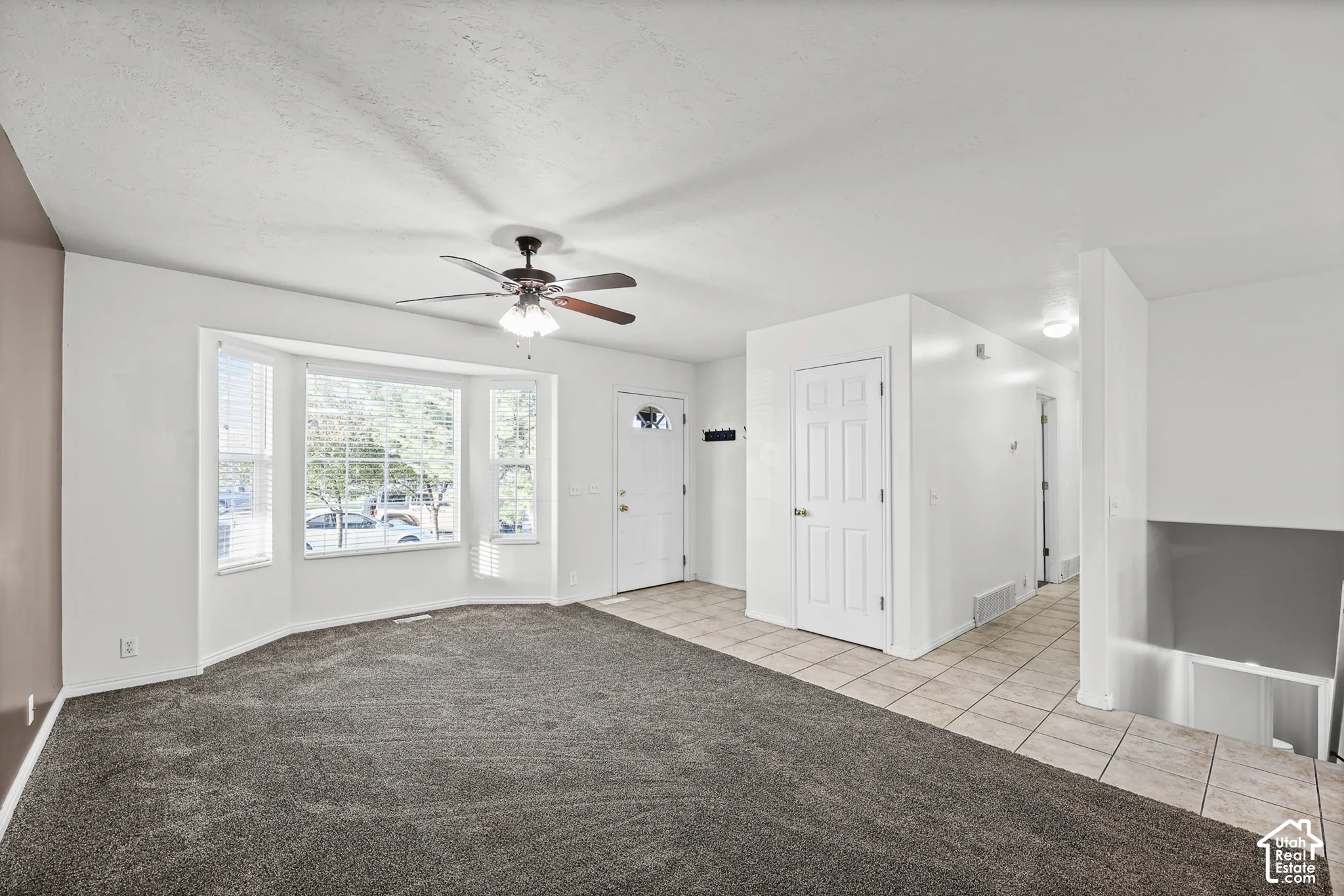 Bay window with blinds, ceiling fan with light fixture, neutral carpet, tiled flooring, and a paneled entry door