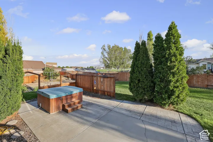 Backyard featuring a hot tub with wood surround, concrete patio, expansive lawn area, mature privacy trees, and wood fencing