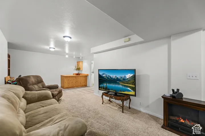Carpeted flooring, recessed lighting, built-in electric fireplace, light wood-finish bar, and tiled flooring