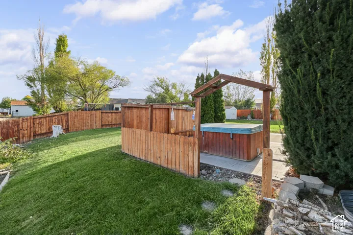 Expansive backyard featuring a hot tub with wood-finish surround, wood privacy fencing, and a manicured lawn