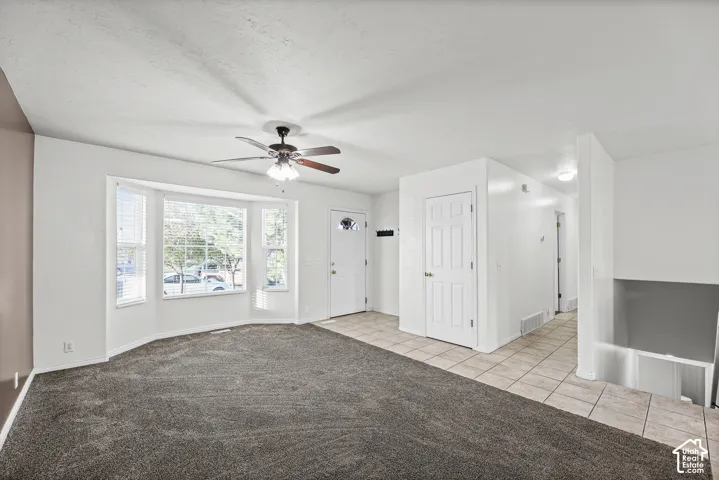 Bay window with blinds, ceiling fan with light fixture, neutral carpet, tiled flooring, and a paneled entry door