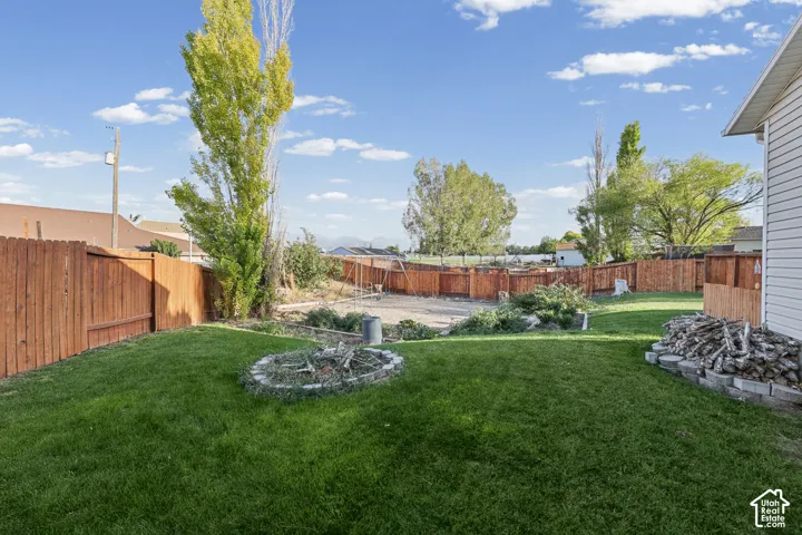 Expansive backyard featuring a green lawn, privacy fencing, and a built-in fire pit