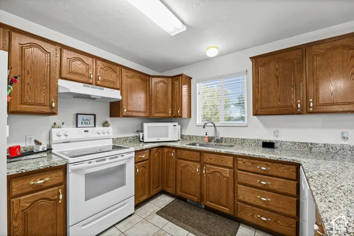 Kitchen featuring wood-finish cabinetry, granite-pattern countertops, white appliances, and tiled flooring