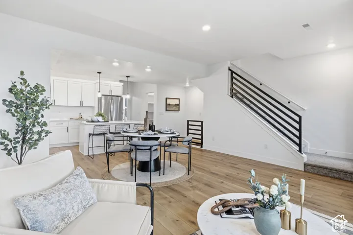 Open-concept living area featuring wood-finish flooring, a modern staircase with horizontal metal balusters, and recessed lighting