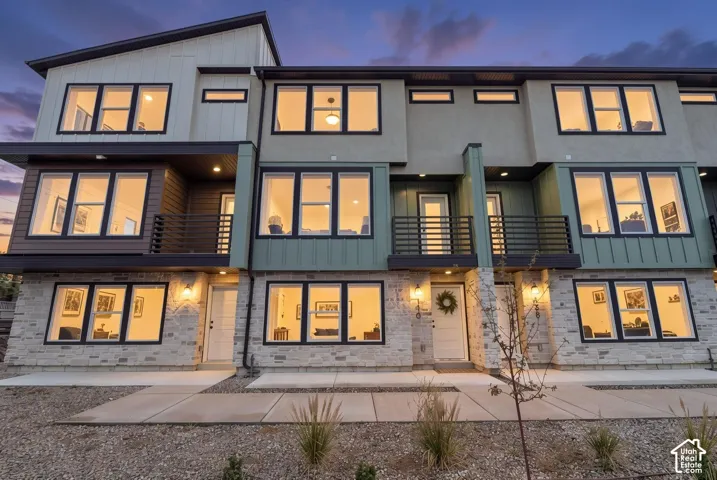 Modern architectural design featuring multiple balconies, mixed material facade with stone accents, dark-framed windows, and exterior lighting fixtures