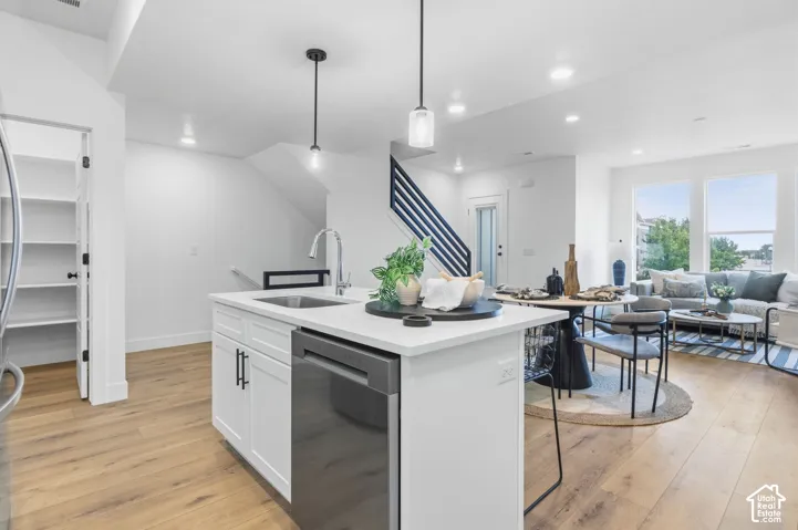 Kitchen island featuring a stainless steel sink, integrated dishwasher, and white cabinetry with dark hardware