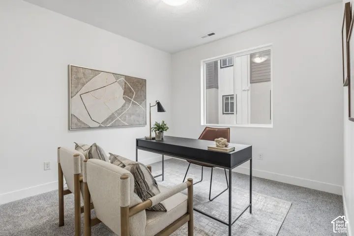 Recessed lighting illuminates the room, featuring a large window, broad white trim, and light gray carpeting