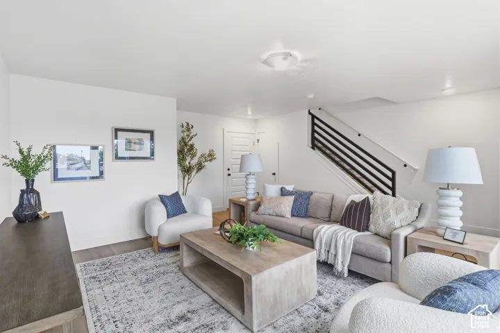Open-concept living area with wood-finish flooring, white walls, and a contemporary black metal stair railing