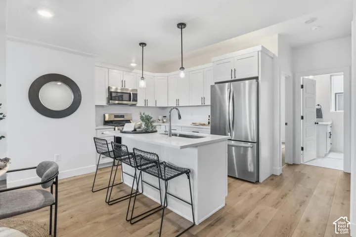 Kitchen featuring white cabinetry, stainless steel appliances, a center island with pendant lighting, light wood-finish flooring, and white countertops