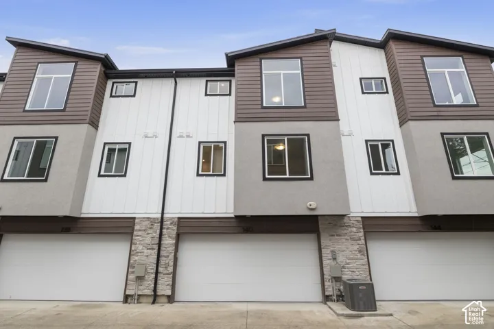 Modern multi-level townhome featuring white siding, brown-hued horizontal siding, and grey stucco exterior