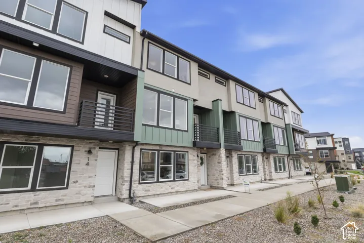 Modern multi-level townhome featuring a stone facade, prominent windows, and a private balcony with horizontal railings