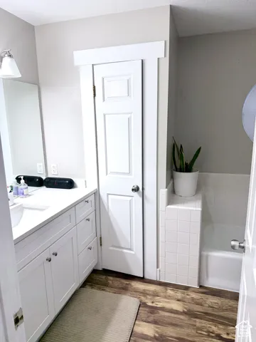 White vanity with a single basin sink, wood-finish flooring, and a tiled bathtub surround