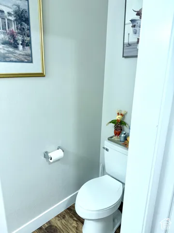 White toilet with a round bowl and a polished chrome toilet paper holder, set against light-colored walls and wood-finish flooring