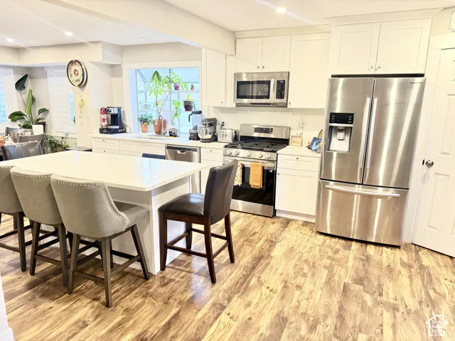 White shaker cabinetry, stainless steel appliances, wood-finish flooring, white countertop, and a center island