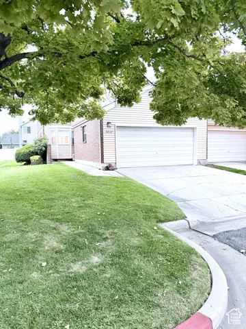 Brick and siding exterior, attached garage, well-maintained lawn, established trees, and a concrete driveway